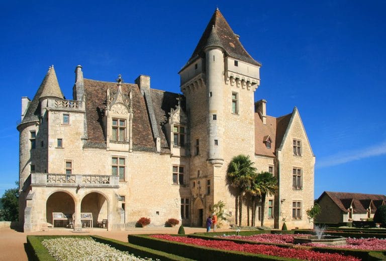 Château historique en pierre avec jardin fleuri.